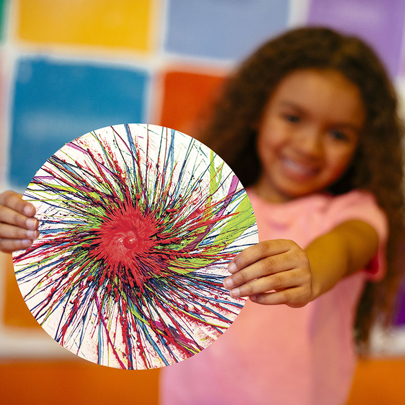 Child holds out a colorful drip art masterpiece